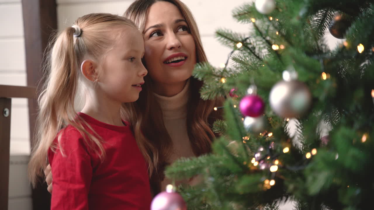 Mother With Her Daughter Hanging Christmas Ornaments On Christmas Tree 3