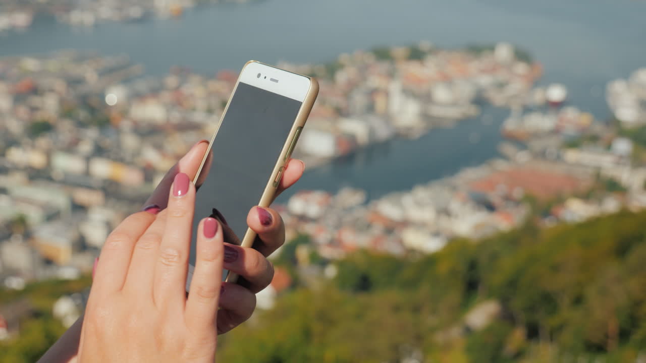 manos femeninas con un teléfono inteligente usan el teléfono contra el fondo de la ciudad de bergen video 4k