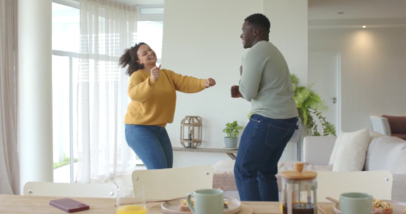 Un couple afro-américain mimant un appel téléphonique, dansant joyeusement à la maison, avec une table à manger et un téléphone.