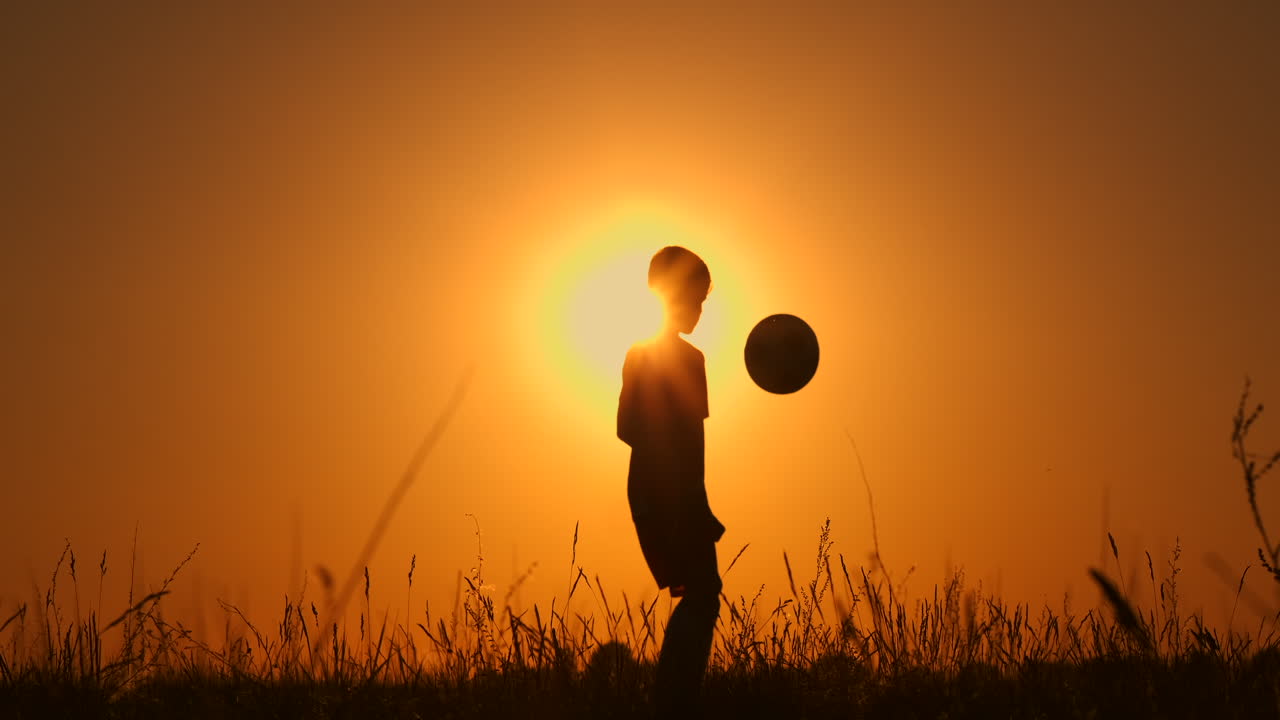 un joven jugador de fútbol se entrena jugando con una pelota metida en su pierna al atardecer en cámara lenta durante la hora dorada en el campo hasta el atardecer. entrenamiento desde el anochecer hasta el amanecer. concepto camino al éxito