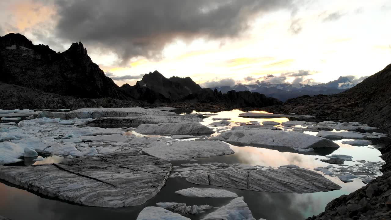 воздушный полет над туристом с видом на ледниковое озеро, полное растаявших айсбергов, в отдаленных районах швейцарских альп на фоне заката за горными вершинами