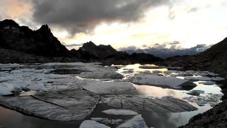 sobrevuelo aéreo sobre un excursionista con vistas a un lago glaciar lleno de icebergs derretidos en partes remotas de los alpes suizos como puestas de sol detrás de los picos de las montañas