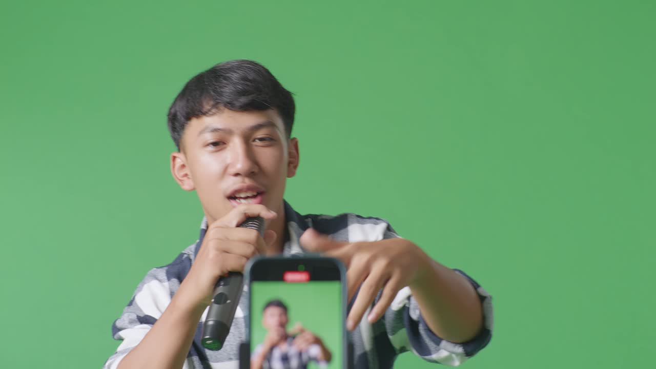 스마트폰 기록의 클로즈업 젊은 아시아 십대 소년 마이크를 들고 녹색 화면 배경에