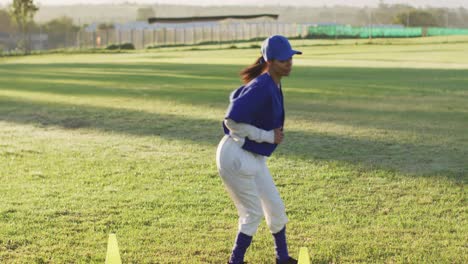 grupo diverso de jugadoras de béisbol ejercitándose en el campo, corriendo entre los conos