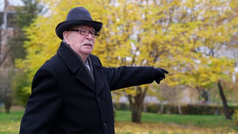 senior man in a black coat and hat in an autumn park