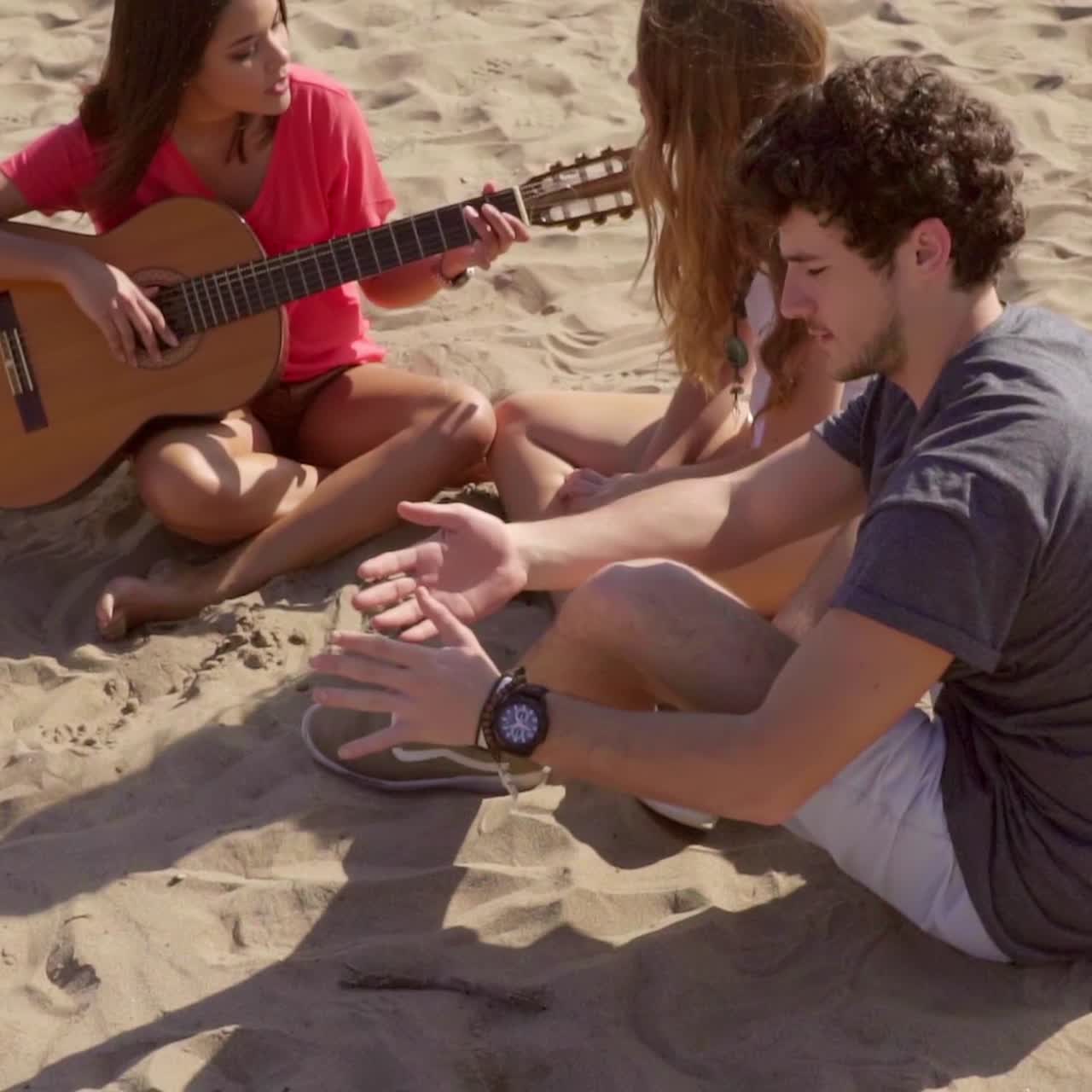 jóvenes amigos relajándose en una playa tocando la guitarra