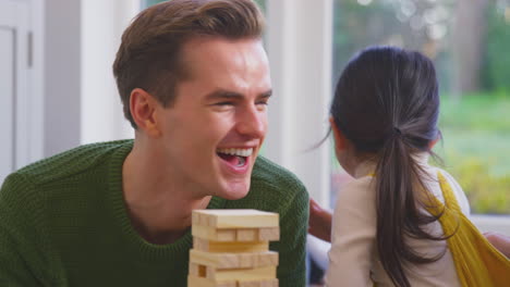 daughter whispering in parent's ear as family with two dads play game stacking wooden bricks