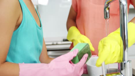 Mother-and-daughter-washing-crockery-in-kitchen-