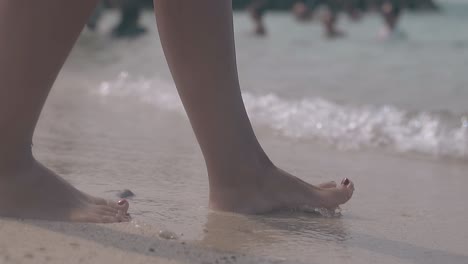 woman-walks-on-sand-and-waves-roll-on-against-people-closeup