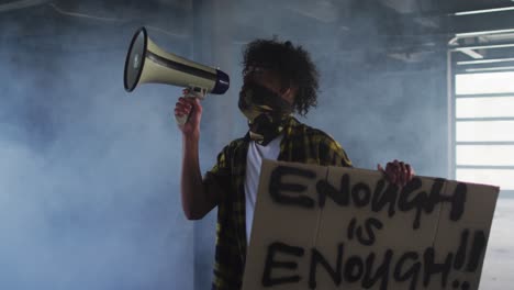 homme afro-américain portant un masque facial parlant dans un mégaphone tenant une pancarte de protestation dans un parking vide