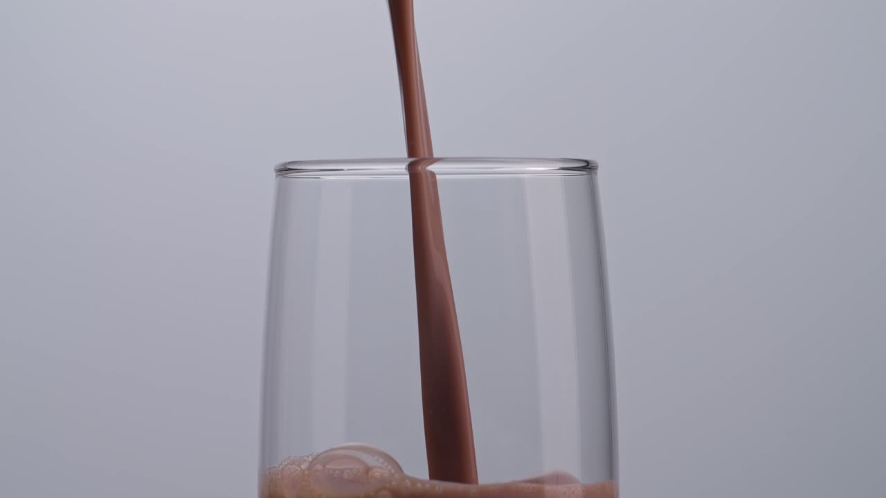 Primo piano di bevanda al latte al cioccolato versata al rallentatore in un bicchiere tumbler su sfondo bianco