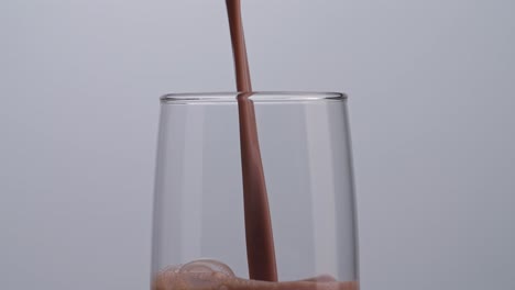 close up of slow motion pour chocolate milk drink in tumbler glass on white background