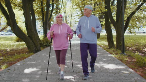 active senior grandparents training nordic walking with ski trekking poles, running in summer park