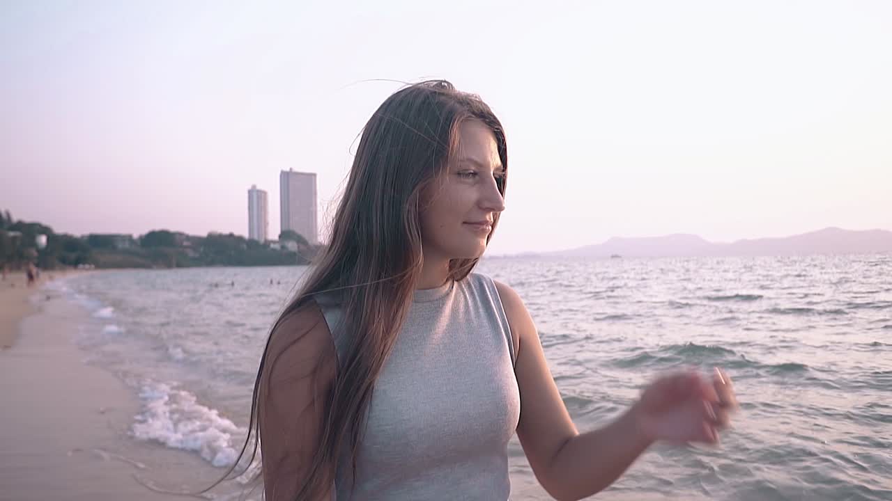 여름 드레스를 입은 우아한 여성이 바다에서 머리카락을 고정시니다.