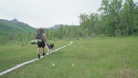 Hombre-Que-Lleva-Una-Gran-Bolsa-De-Camping-Acompañado-Por-Un-Perro-Que-Pasa-Por-La-Pasarela-En-El-Parque-Nacional-De-Ånderdalen-En-La-Isla-De-Senja,-Noruega