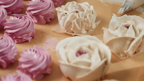 close up of beautifully arranged pink swirl cupcakes and flower-shaped white frosting cakes resting on parchment paper beside piping cone, showcasing homemade dessert artistry