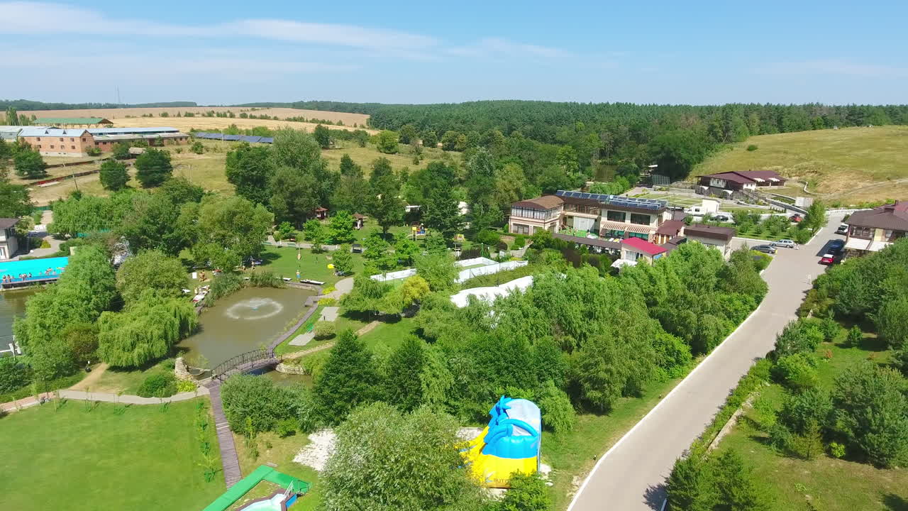 Sunlit green territory of beautiful spa resort in the countryside. Swimming-pool with people resting around it. Aerial perspective.