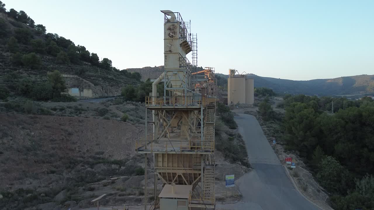 Industrial cement plant with silos and conveyor belts in the midst of a mountainous landscape at twilight