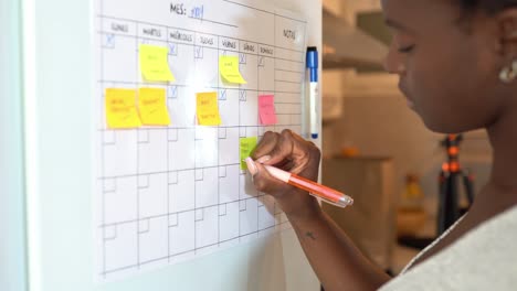 crop black woman taking notes in planner on fridge