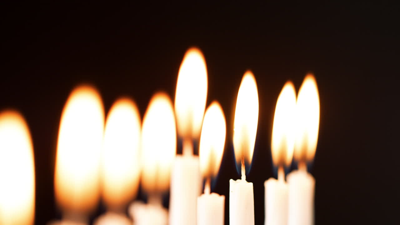 Dettaglio con rack focus delle fiamme su una fila di nove candele bianche che bruciano durante la festa ebraica di Hanukkah
