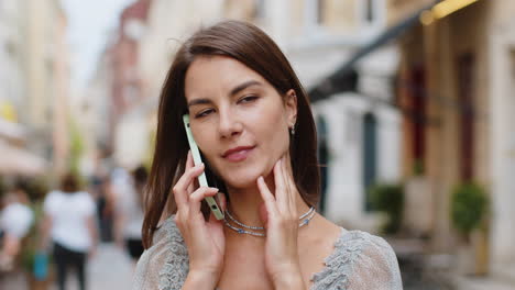 mujer joven feliz teniendo una conversación remota hablando en el teléfono inteligente, buenas noticias chismes en la calle de la ciudad