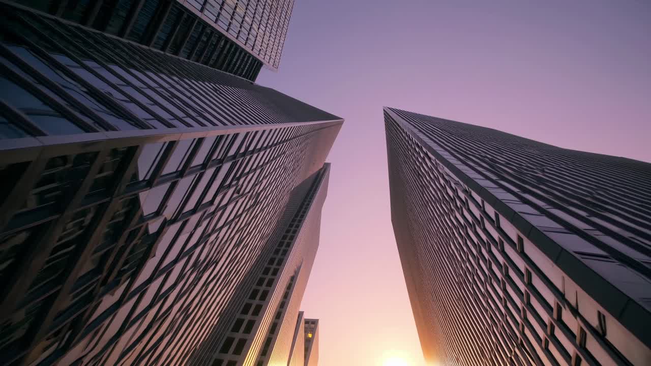 Low-angle video shot of modern skyscrapers at sunset, capturing sleek, reflective surfaces