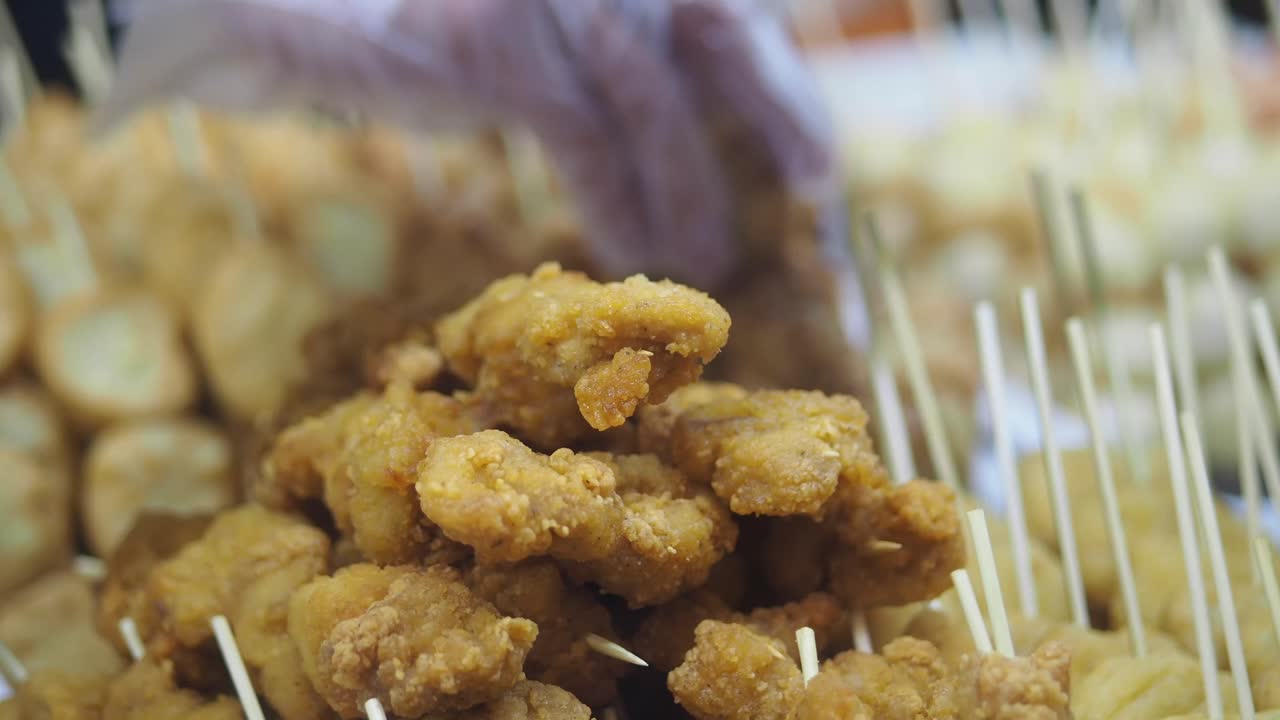 Primo piano di spiedini di pollo fritto dorati in una bancarella di cibo.