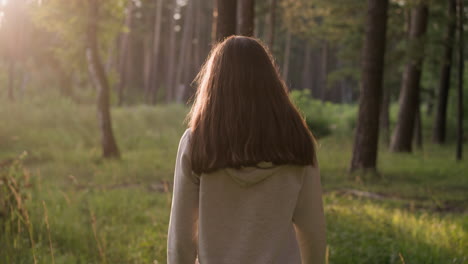 lonely woman walking through sunny forest. female walks alone surrounded by trees and wild environment at sunset. lady feels empty and useless