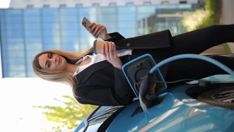 a dynamic video showing a woman in a business suit charging a blue electric car and using her phone. highlighting the modern and ecofriendly concept of electric vehicles