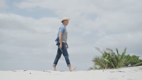 Happy-senior-caucasian-man-walking-barefoot-on-tropical-beach,-in-slow-motion