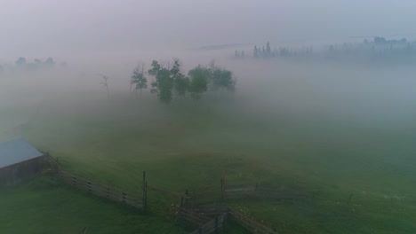 low visibility aerial view through fog and smoke over a barn, pasture and fences on a rural alberta farm