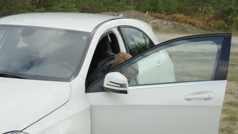 Trendy-young-male-in-leather-jacket-gets-out-of-a-white-car-forest-background