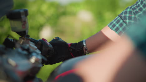 primer plano de la mano de un motociclista que usa guantes de protección mientras acelera la motocicleta, una cadena de muñeca es visible en la muñeca del piloto, y el fondo está borroso