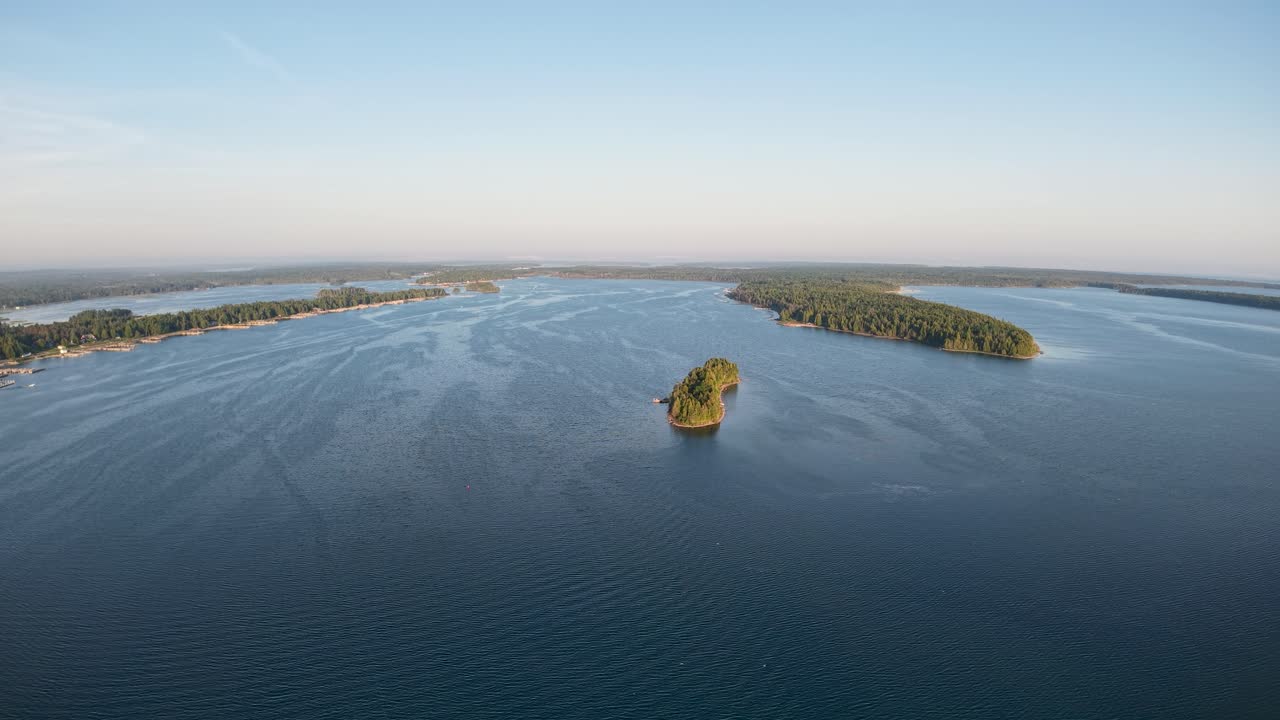 Aerial drone footage of a small forested island surrounded by open blue water in Michigan’s Upper Peninsula, Les Cheneaux Islands