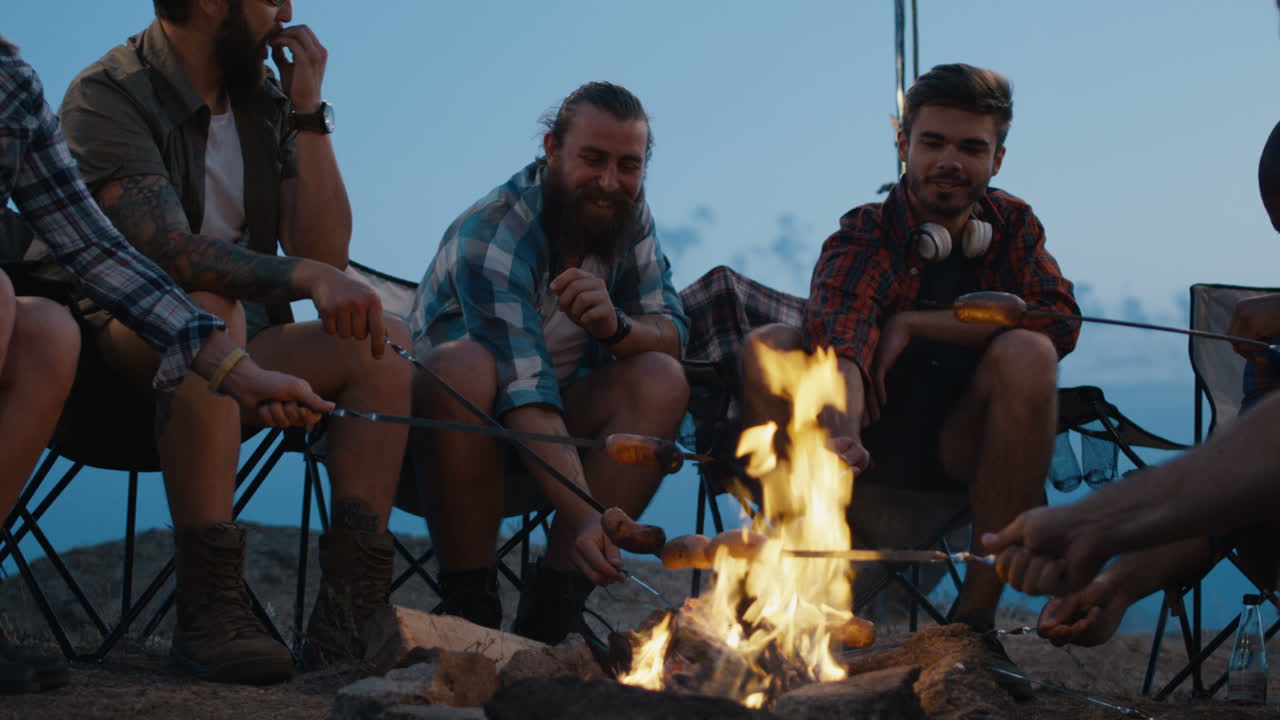 Friends Roasting Sausages by Campfire