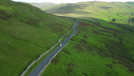 following mountain pass road with traffic amongst green hills on summer day