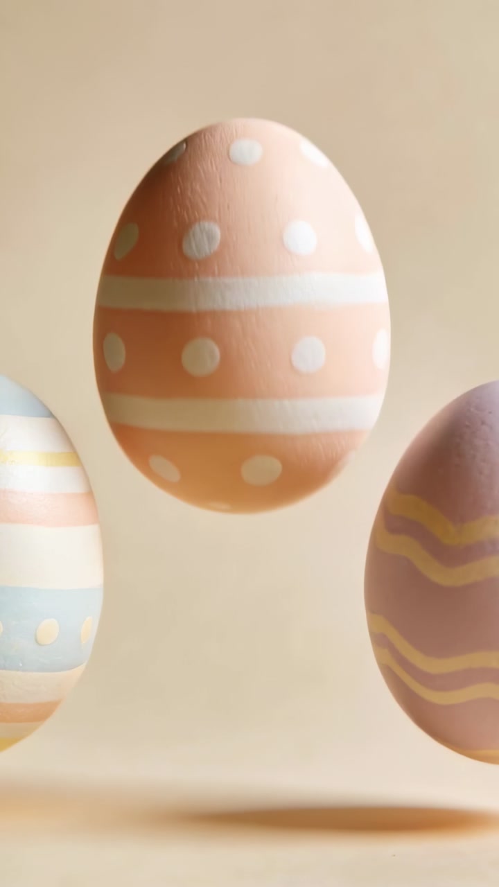 Vertical video: Bobbing peach polka-dot egg landing, tilting on beige table as side eggs slide in