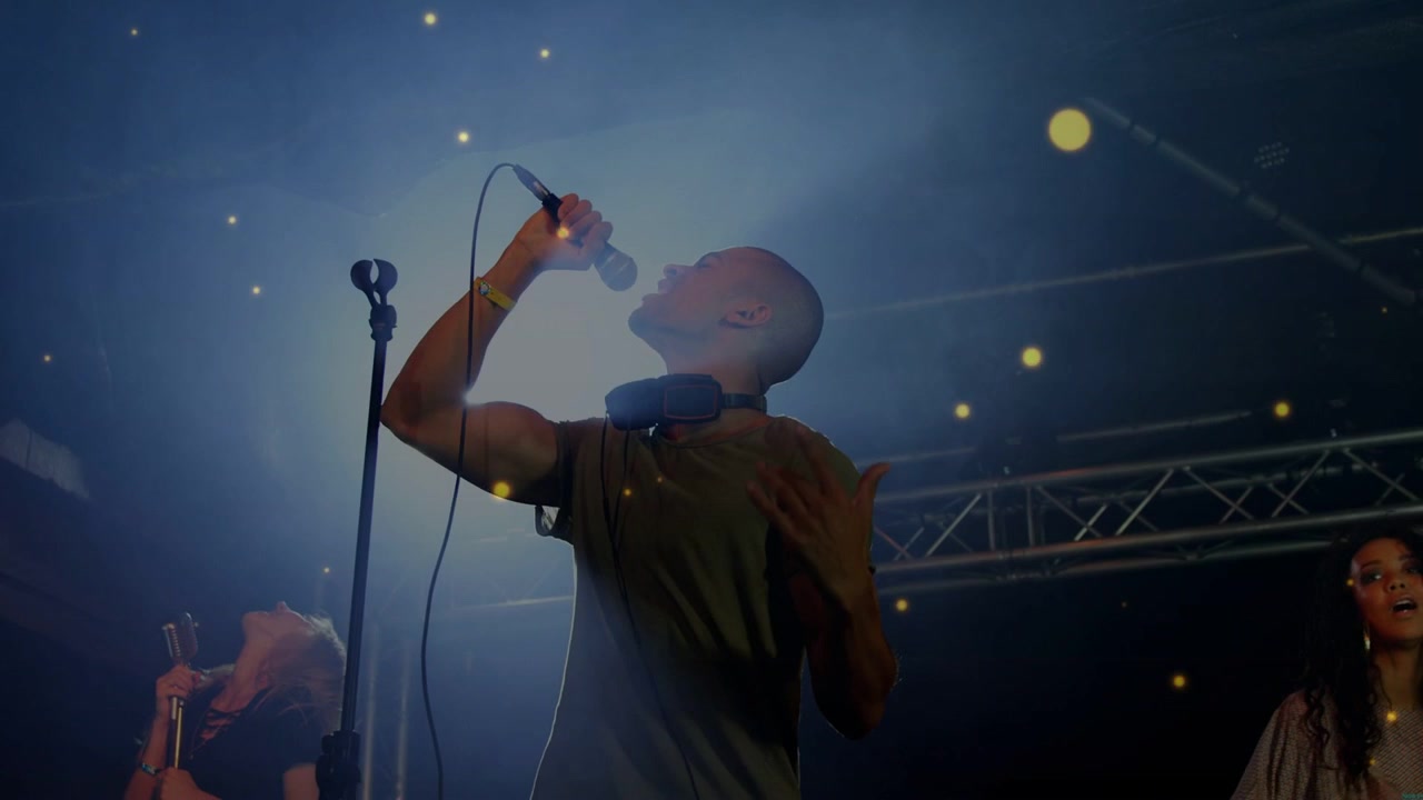 Vokalist synger på musikksted, spotlight-bluss vokser og gullpartikler skjuler trioen.
