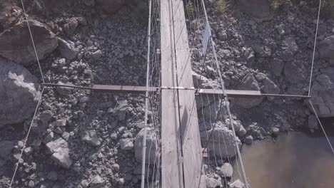 pov aerial: well-built, scary narrow suspension bridge in river canyon