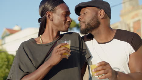 retrato de gays despreocupados besándose y bebiendo jugo afuera