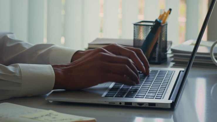 Hände eines männlichen Solopreneurs, der am Schreibtisch auf einem Laptop tippt