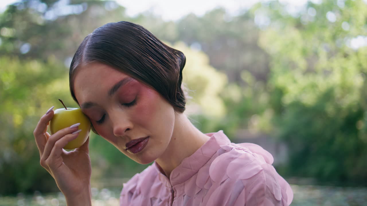 미스터리한 여자가 사과를 들고 있는 카메라를 쳐다보고 있다. 요정 소녀가 자연을 포즈를 취하고 있다.