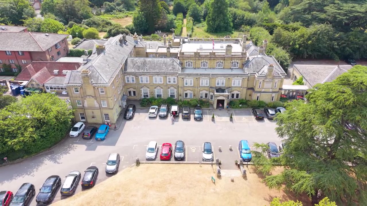 Chilworth Manor vicino a Southampton, Inghilterra. Il drone si alza e si allontana dalla facciata anteriore del maniero georgiano, rivelando il parcheggio e i giardini durante l'estate, con erba secca e un parcheggio affollato.