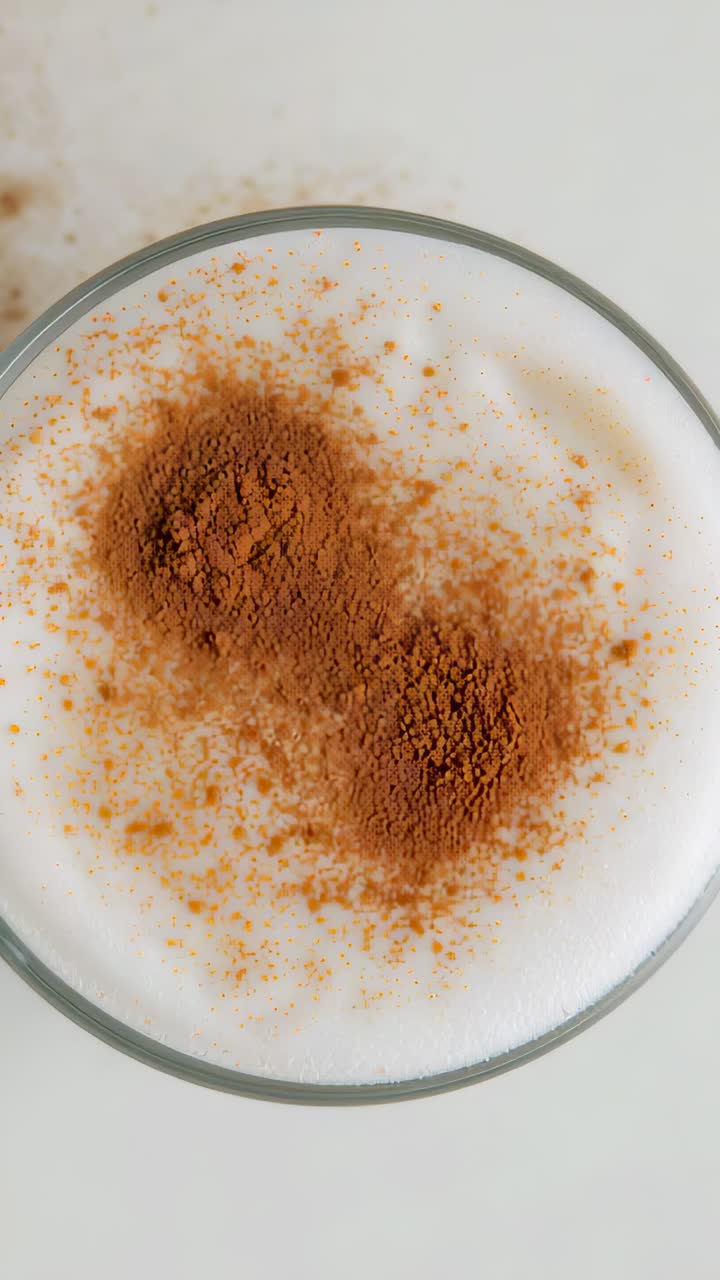 Vertical video: Pouring shaker sliding in, sifting spice onto glass of milk foam at home to garnish