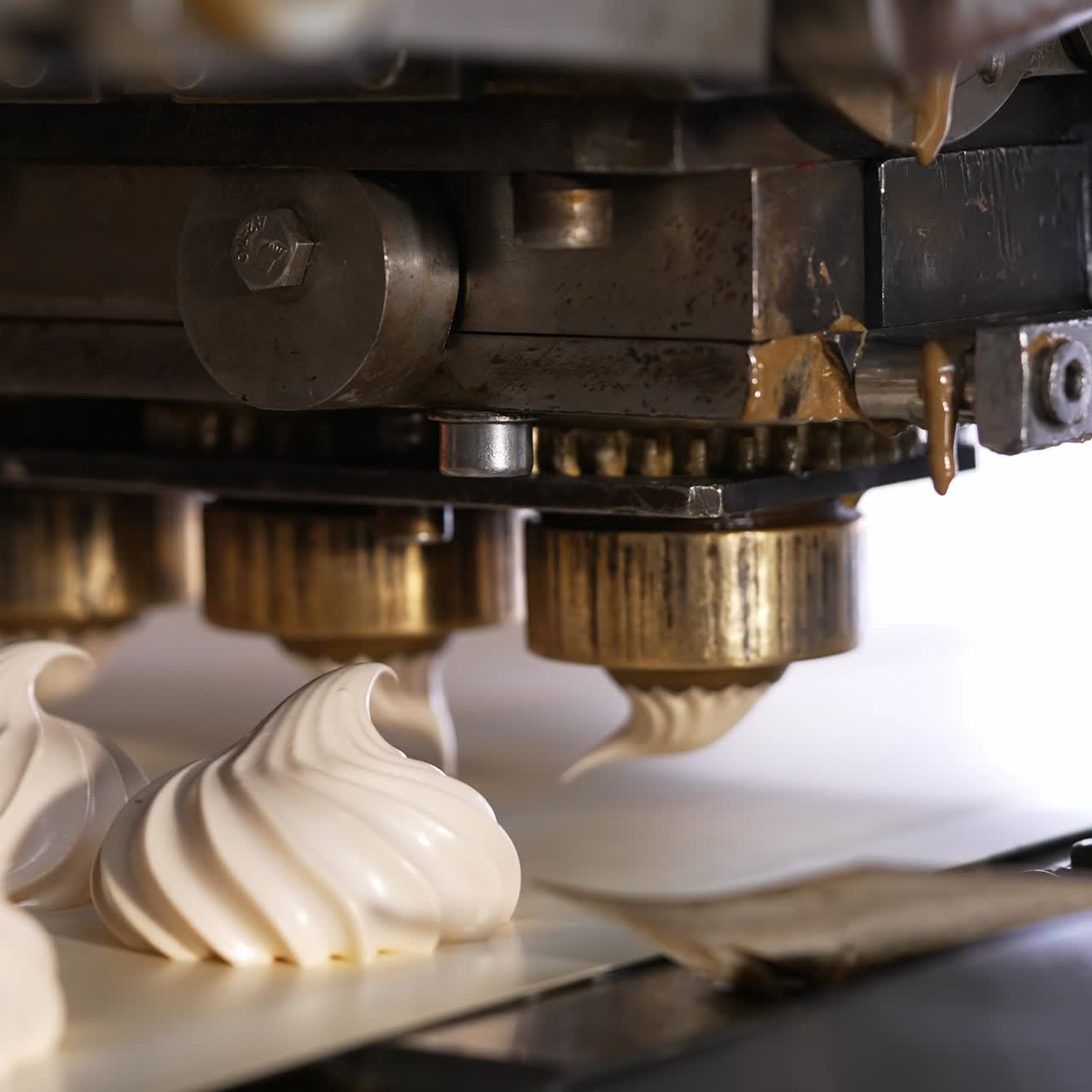 Few metal nozzles rotate and squeeze creamy marshmallows on conveyor belt. Automated line for desserts manufacturing. Close up