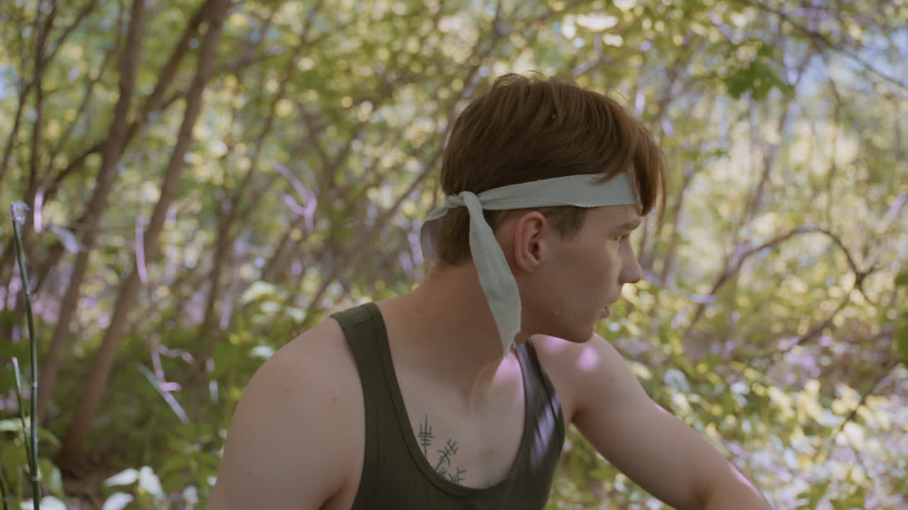 Soldier bends his head and ties the head band, preparing like soldier ready for a fight and action in the forest, focused and determined, with clear intention in an intense outdoor setting