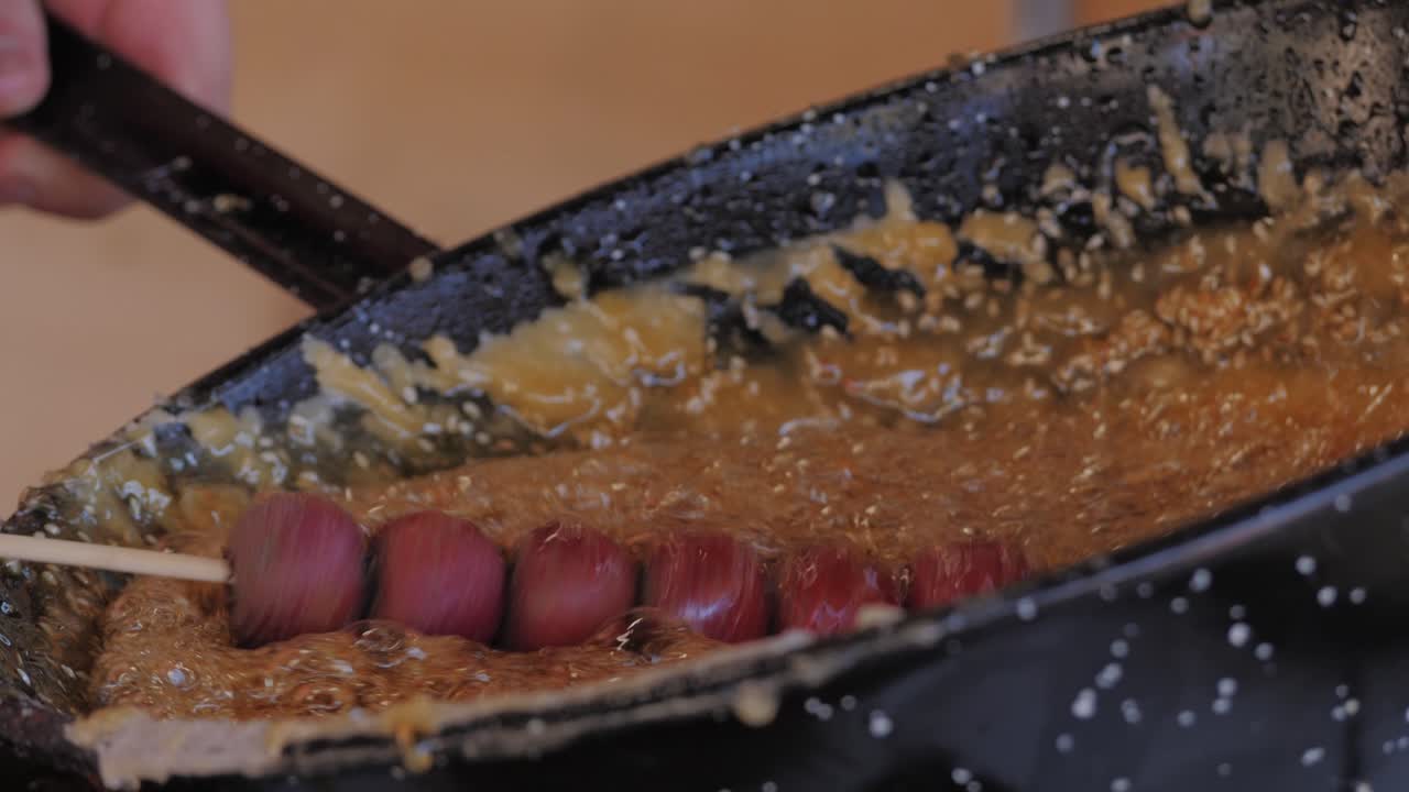 Primo piano di zucchero bollente con bolle che si trasforma in caramello in una pentola nera, caramellizzazione, chef che prepara un dessert in un bar, cibo da pasticceria di un ristorante. Dessert invernale cinese Tanghulu. Frutta caramellata nello zucchero. Concetto di mercato dello street food