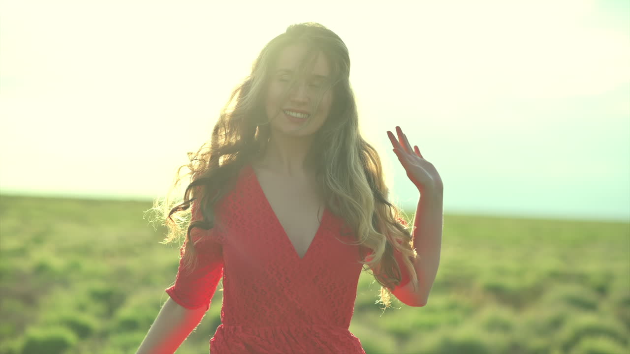 A joyful woman in a red lace dress spins gracefully in a sunlit field
