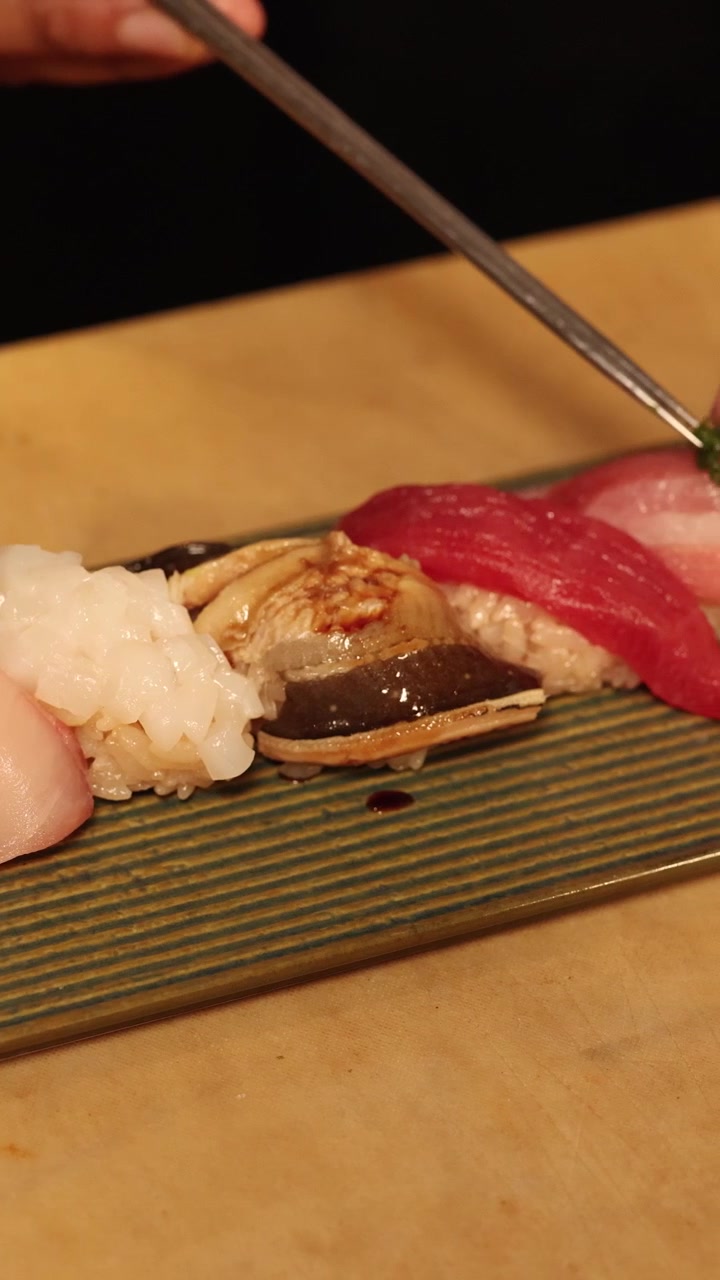 En kok bruger metaltænger til forsigtigt at pynte en række friske nigiri sushi-stykker