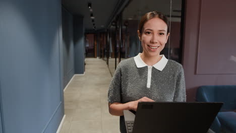 Professional Woman Using Laptop in Modern Office Hallway